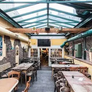 Large interior area of Sowiso Ocean Bar with wooden tables, wooden chairs and glass roof